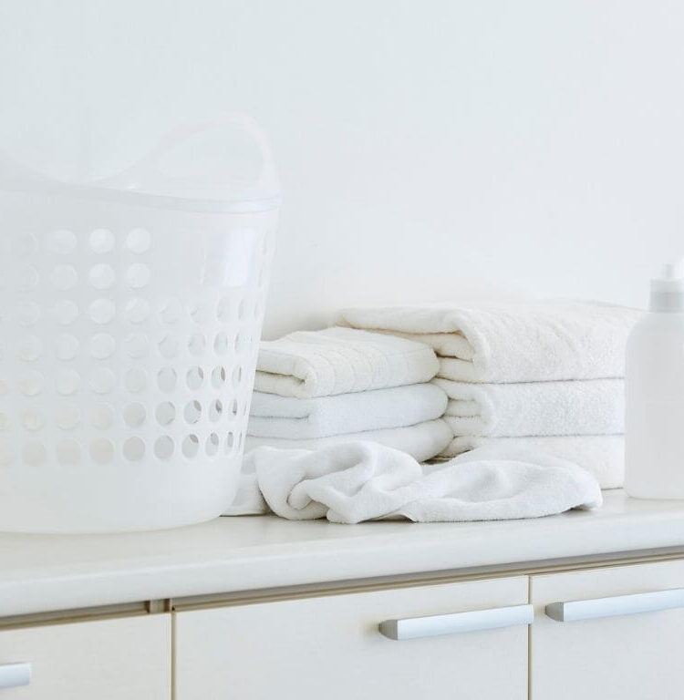 Stack of clean bath towels on a white dresser with a bottle of natural laundry detergent