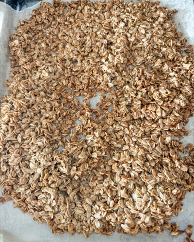 Close up of cooked homemade granola on top of brown parchment paper on top of a stainless steel cookie sheet.
