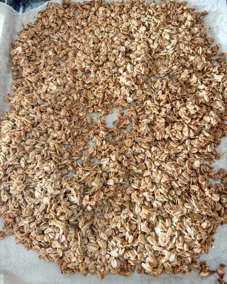 Close up of cooked homemade granola on top of brown parchment paper on top of a stainless steel cookie sheet.