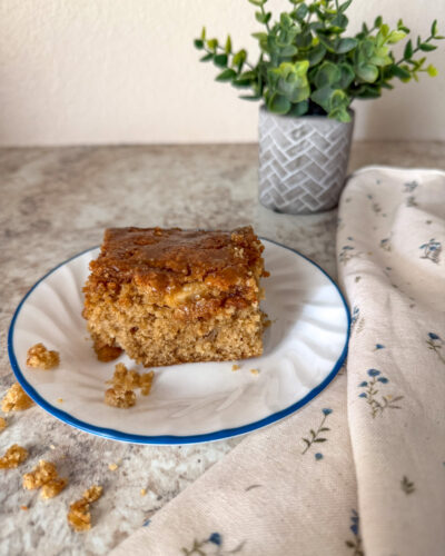 apple cake on plate on top of a neutral colored kitchen counter with a floral kitchen towel next to it