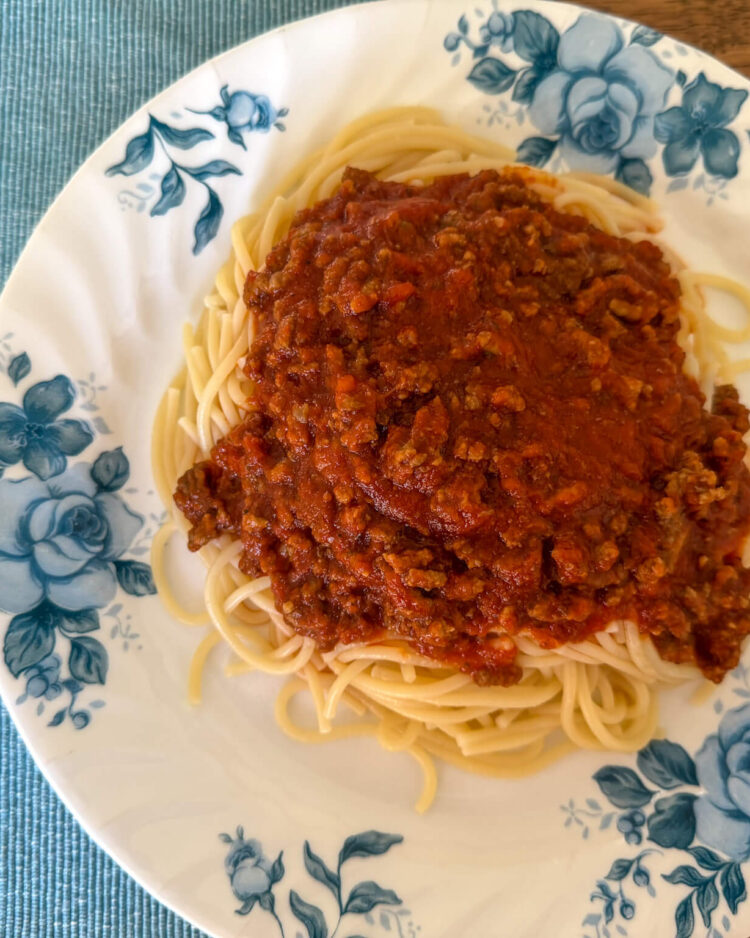How to Make Spaghetti Sauce Thicker. Plate of spaghetti topped with rich tomato sauce, served on a white dish with blue flowers.