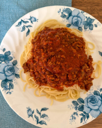 How to Make Spaghetti Sauce Thicker. Plate of spaghetti topped with rich tomato sauce, served on a white dish with blue flowers.