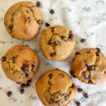 Five einkorn flour sour cream chocolate chip muffins arranged sideways on a neutral floral background