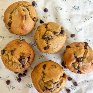 Five einkorn flour sour cream chocolate chip muffins arranged sideways on a neutral floral background