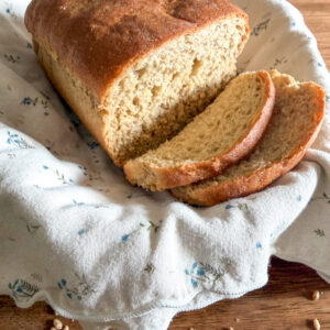 Fresh milled bread with Khorasan and hard white wheat in a basket with a neutral colored kitchen towel on top of a wooden table with wheat berries scattered around.