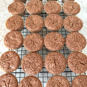 1 dozen chocolate zucchini muffins cooling on a wire baking rack on a neutral colored kitchen counter.