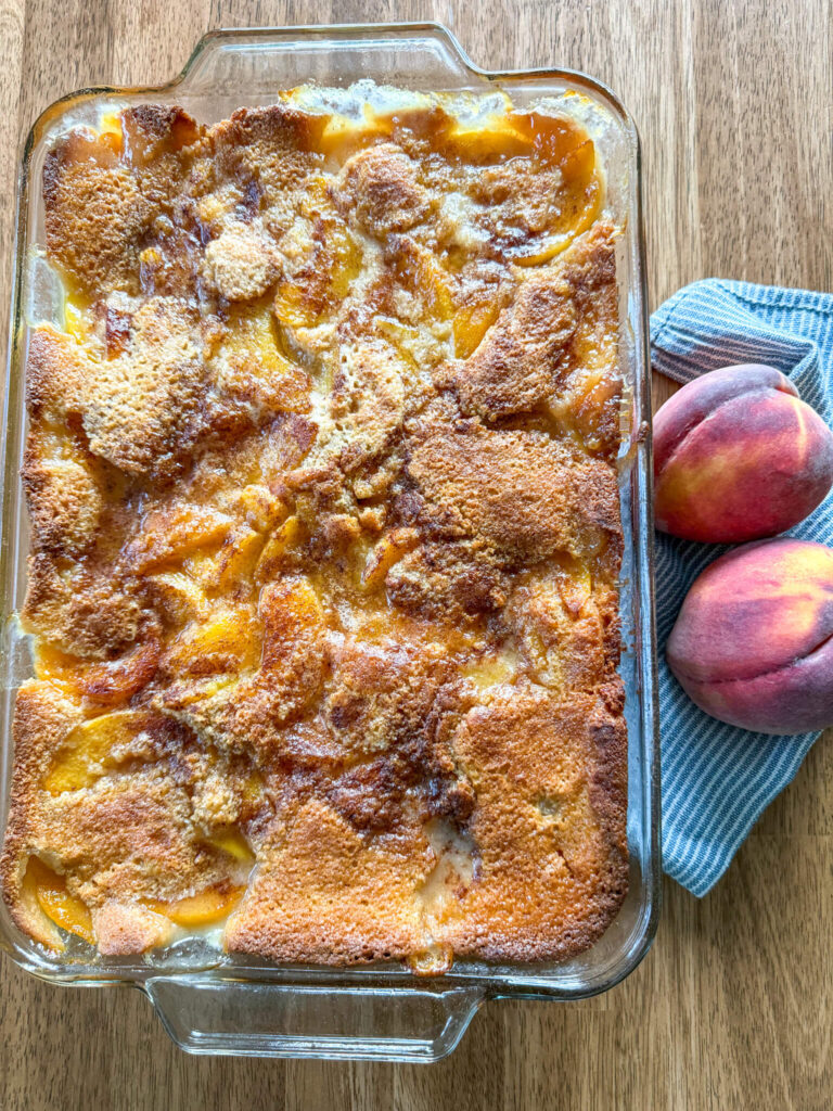 freshly baked peach cobbler recipe with fresh milled flour on wooden table next to two peaches on blue and white striped kitchen napkin