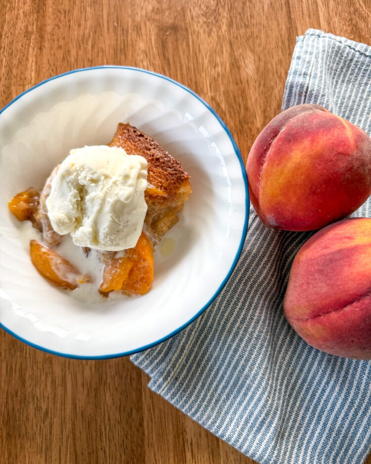a serving of peach cobbler recipe with fresh milled flour in a blue and white bowl with ice cream on top next to a blue and white striped napkin with two peaches on it